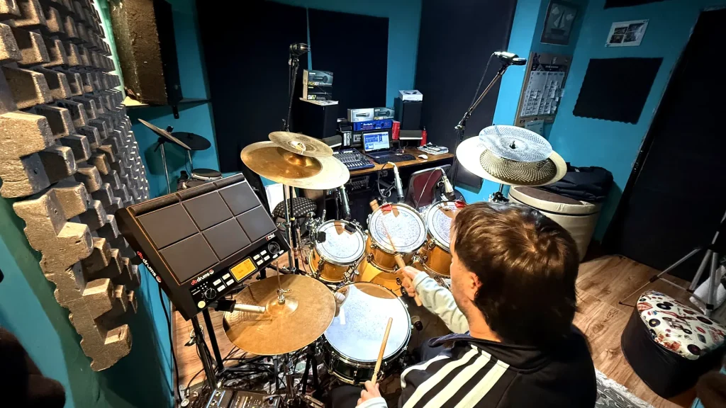 Drummer playing a mic'd drum kit with the DAW recording session visible on screen behind him